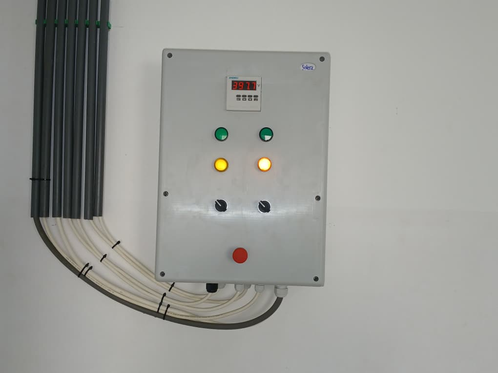 Installed electrical control panel with indicator lights, digital voltage display, and cable conduits